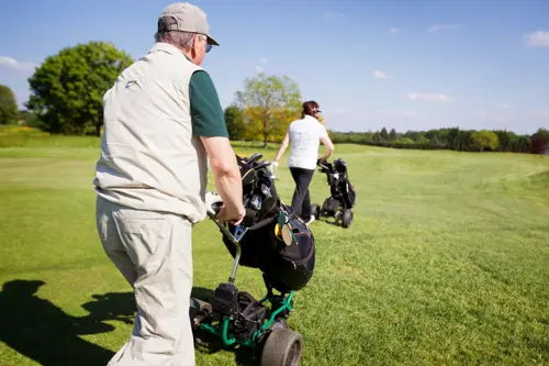 two golfers pushing electric golf trolleys