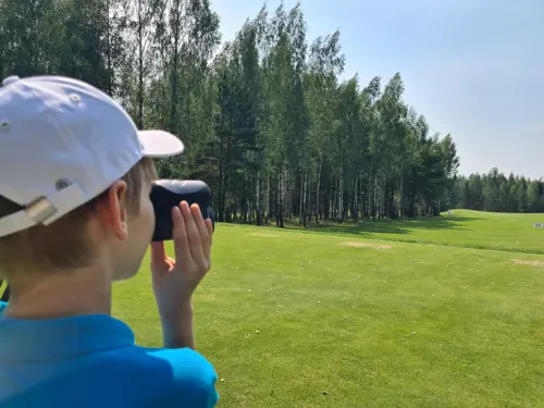 A boy using a rangefinder on the golf course